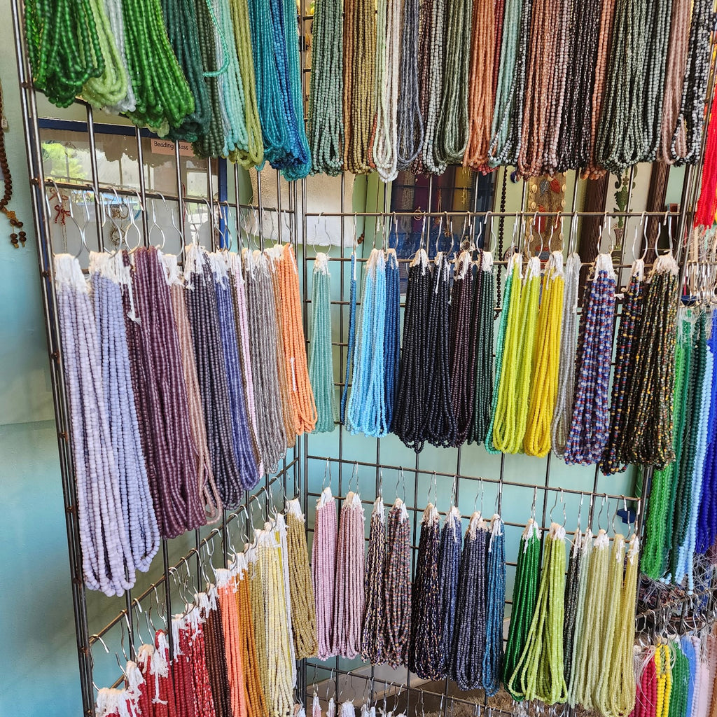 Display of colorful beaded necklaces on a rack against a light blue wall.