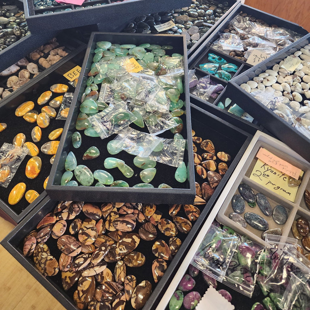 Collection of various colored gemstones in display boxes on a wooden floor.
