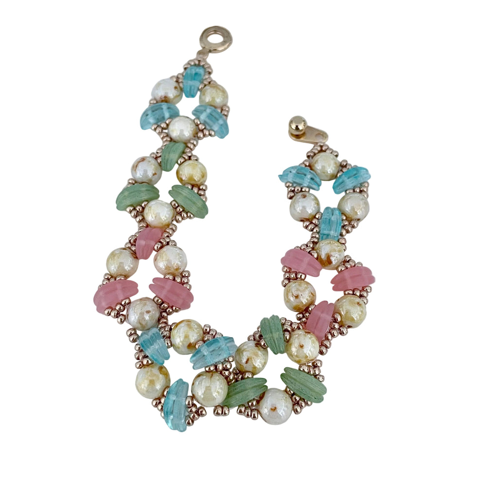A handmade beaded bracelet featuring faux pearls, turquoise, pink, and mint green beads set in rose gold-toned metal, displayed on a light gray background.