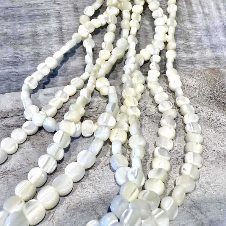 Three strands of white shell beaded necklaces on a wooden surface