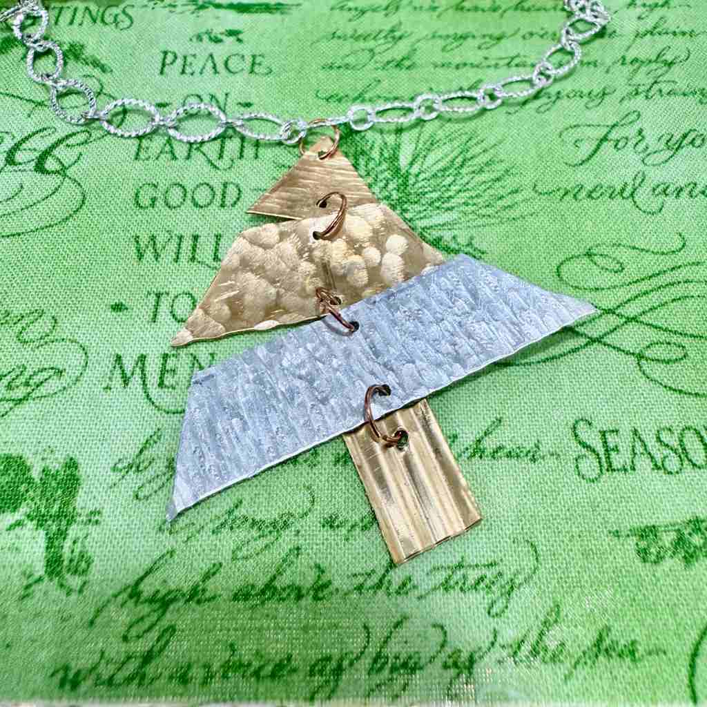 Necklace with geometric pendants shaped like a Christmas tree on a green fabric background with text