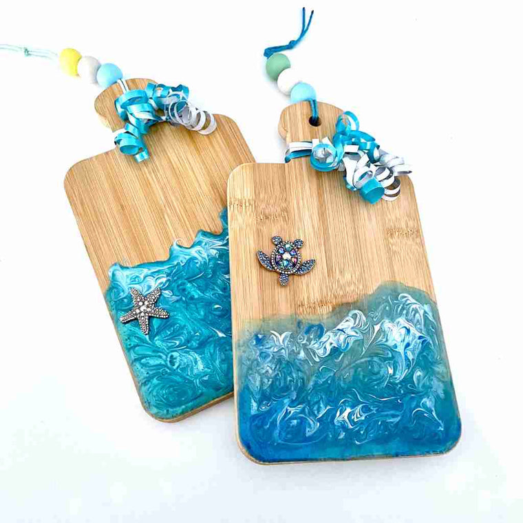 2 decorative cutting boards with ocean colored resin overlay in the shape of the surf with turtle charm