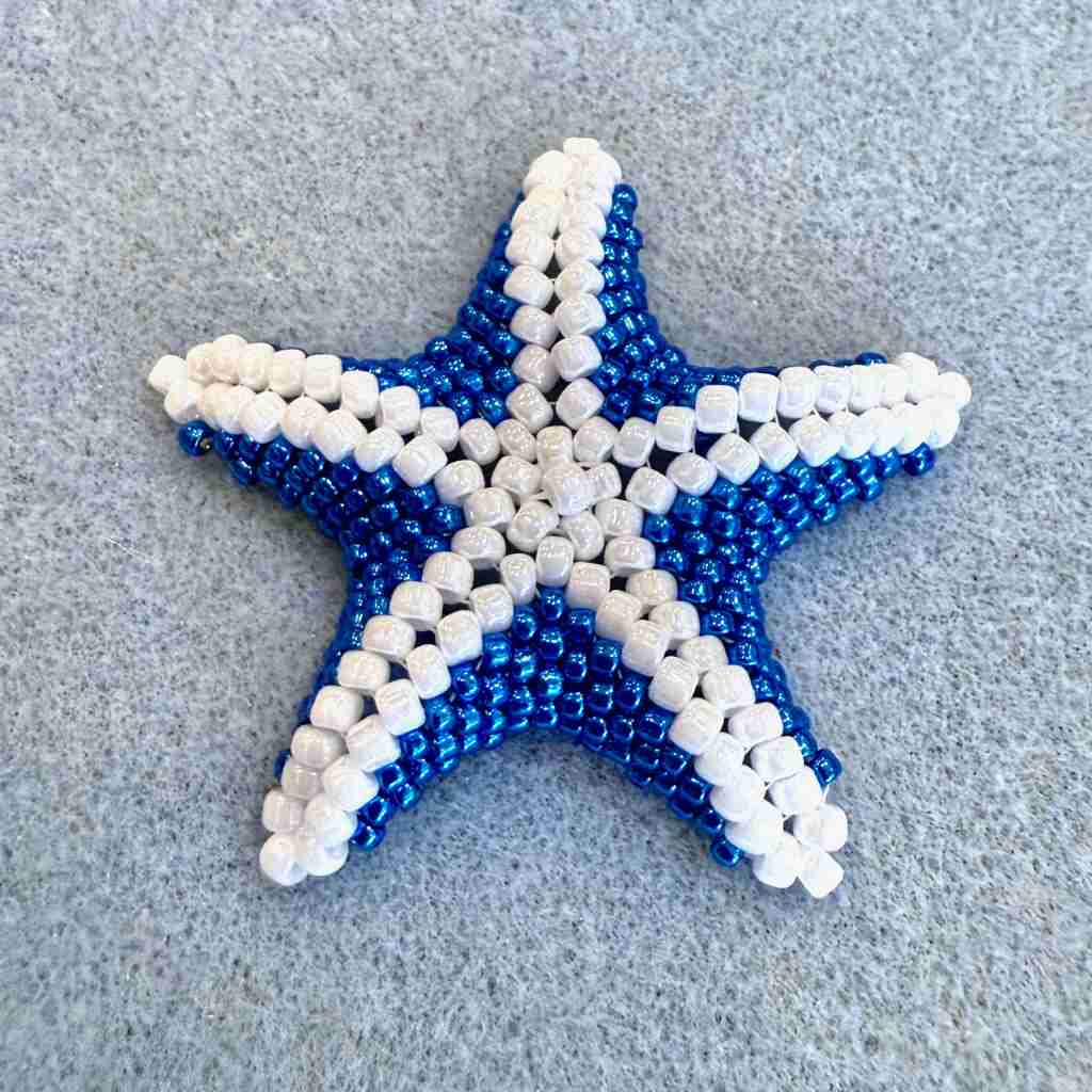 Star-shaped object made of blue and white beads on a textured surface